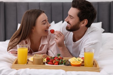 Photo of Tasty breakfast. Happy husband feeding his wife on bed at home