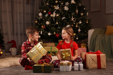 Photo of Cute little children with gift boxes near Christmas tree at home