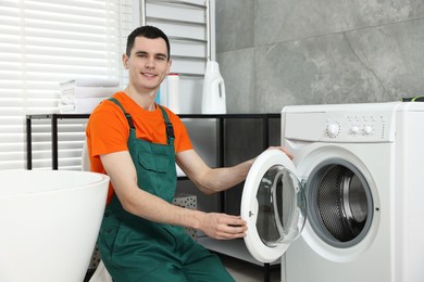 Photo of Smiling plumber repairing washing machine in bathroom