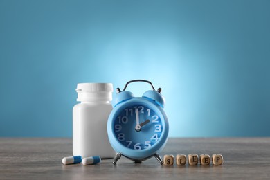 Photo of Word Sleep made of cubes, alarm clock and pills on wooden table. Insomnia treatment