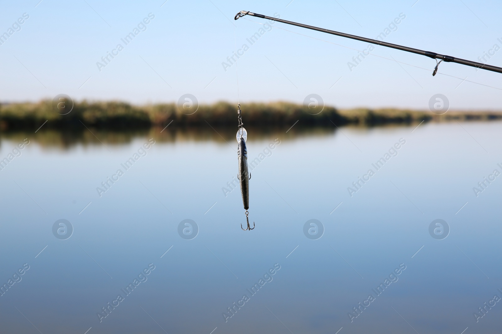 Photo of Fishing rod with lure at riverside on sunny day