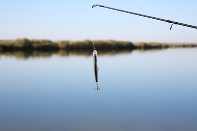 Photo of Fishing rod with lure at riverside on sunny day