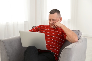 Photo of Mature man with laptop sitting in armchair at home