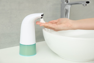 Woman using automatic soap dispenser in bathroom, closeup