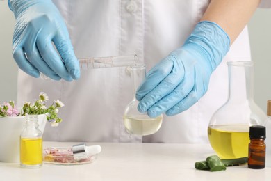 Photo of Scientist developing cosmetic oil at white table, closeup