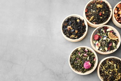 Different kinds of dry herbal tea in wooden bowls on light grey table, flat lay. Space for text