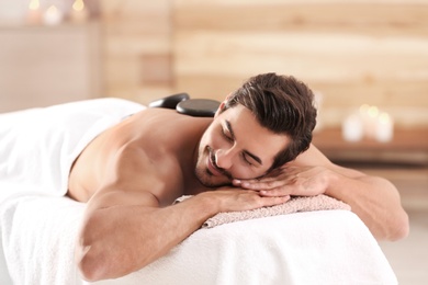Photo of Handsome young man receiving hot stone massage in spa salon