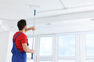 Photo of Handyman painting ceiling with roller in room, back view