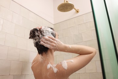 Photo of Woman washing hair while taking shower at home, back view