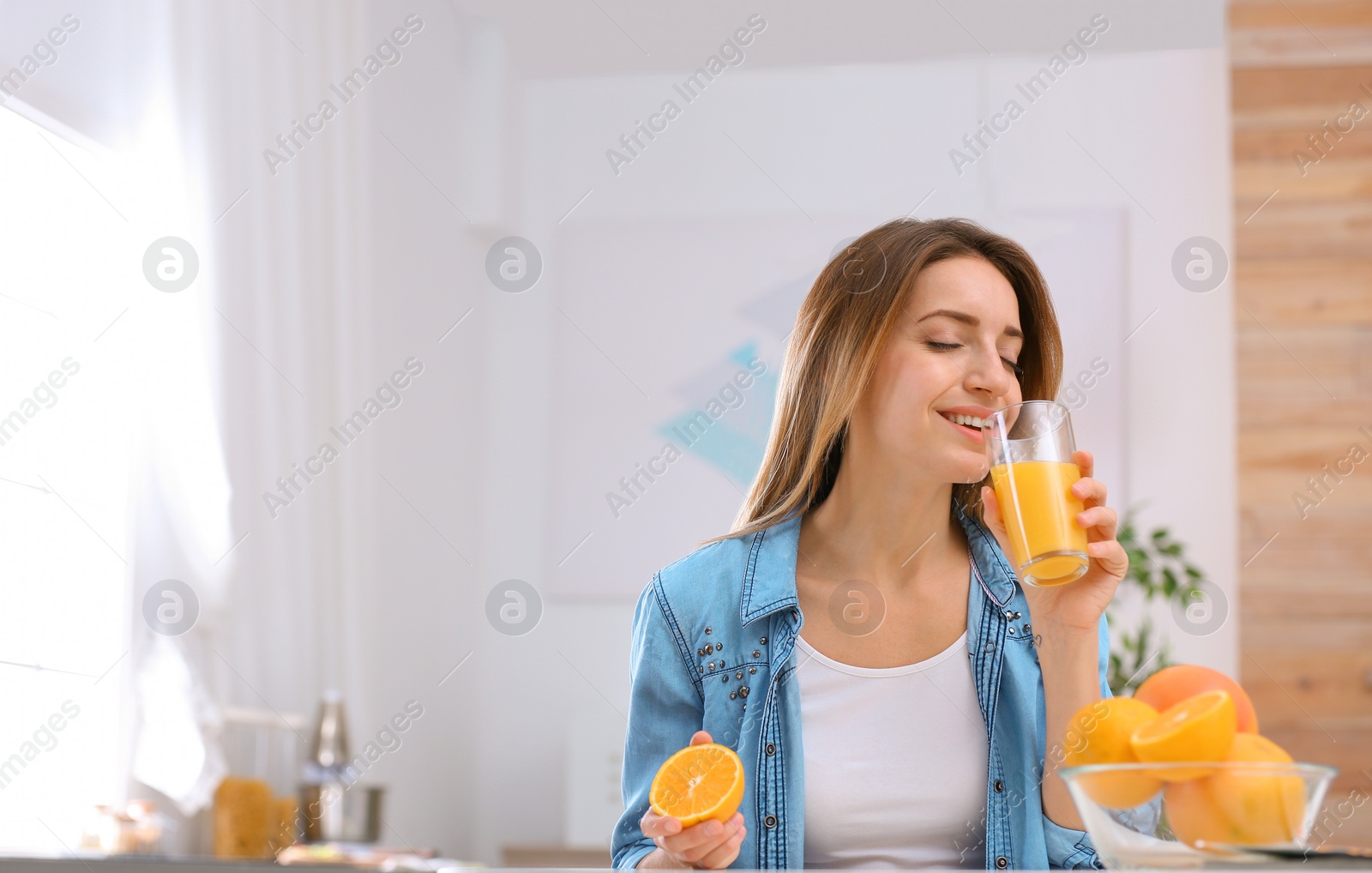 Photo of Beautiful young woman drinking orange juice at table indoors, space for text. Healthy diet