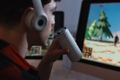 Photo of Young man with energy drink playing video game at wooden desk indoors, closeup