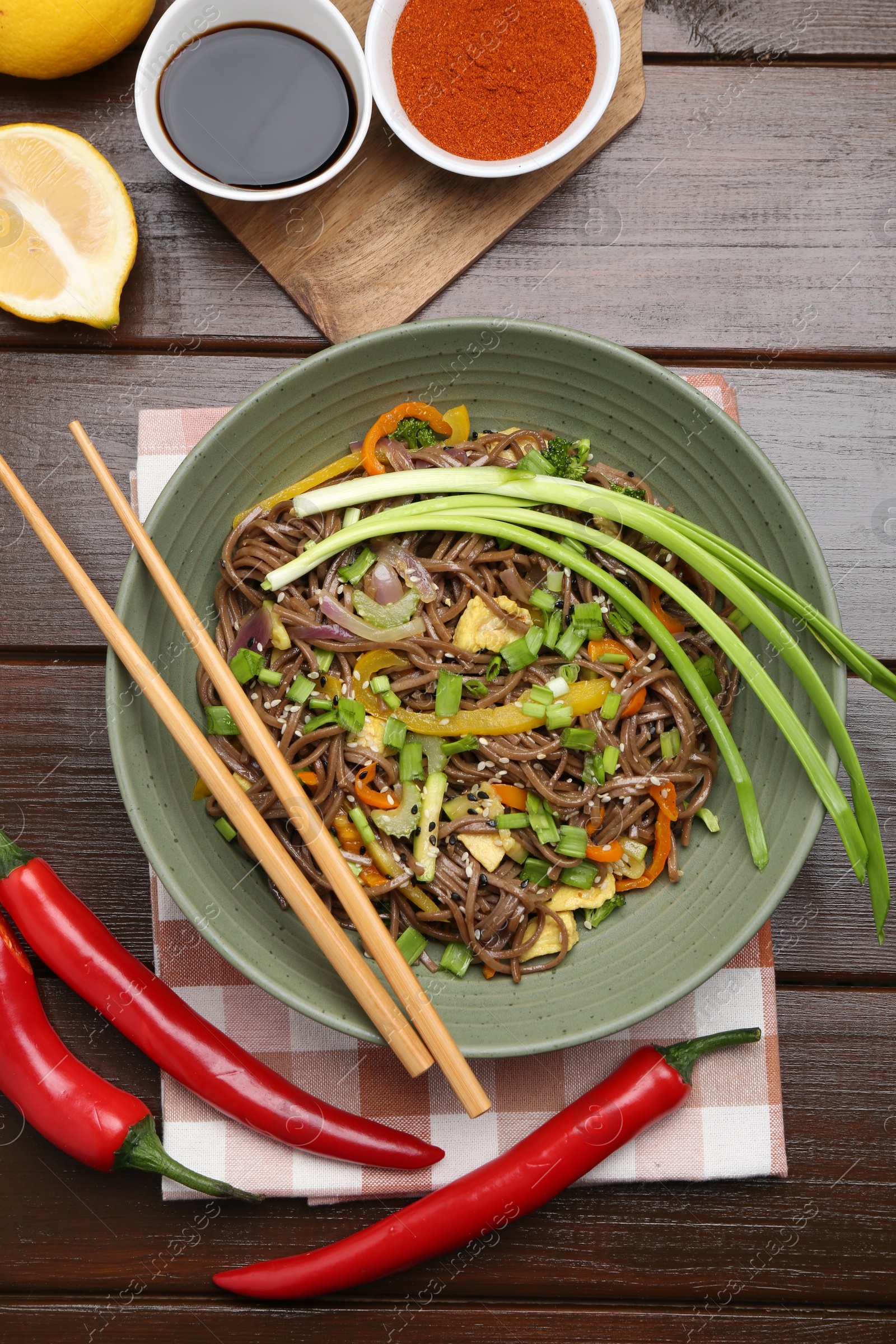 Photo of Stir-fry. Delicious cooked noodles with chicken and vegetables in bowl on wooden table, flat lay