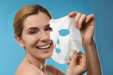 Photo of Beautiful woman with cotton facial mask sheet against color background