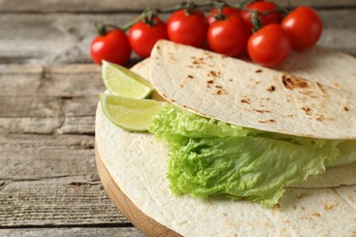 Photo of Tasty homemade tortillas, tomatoes, lime and lettuce on wooden table, closeup