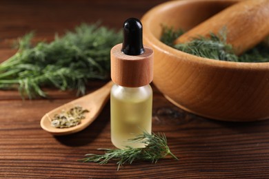 Photo of Bottle of essential oil and fresh dill on wooden table