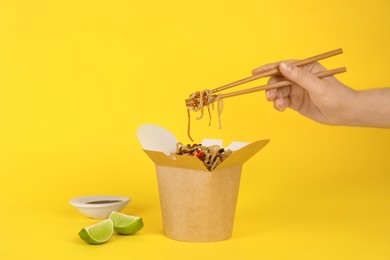 Photo of Woman eating seafood wok noodles with chopsticks from box on yellow background, closeup
