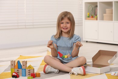 Photo of Cute little girl playing with wooden pieces and string for threading activity indoors. Child's toy