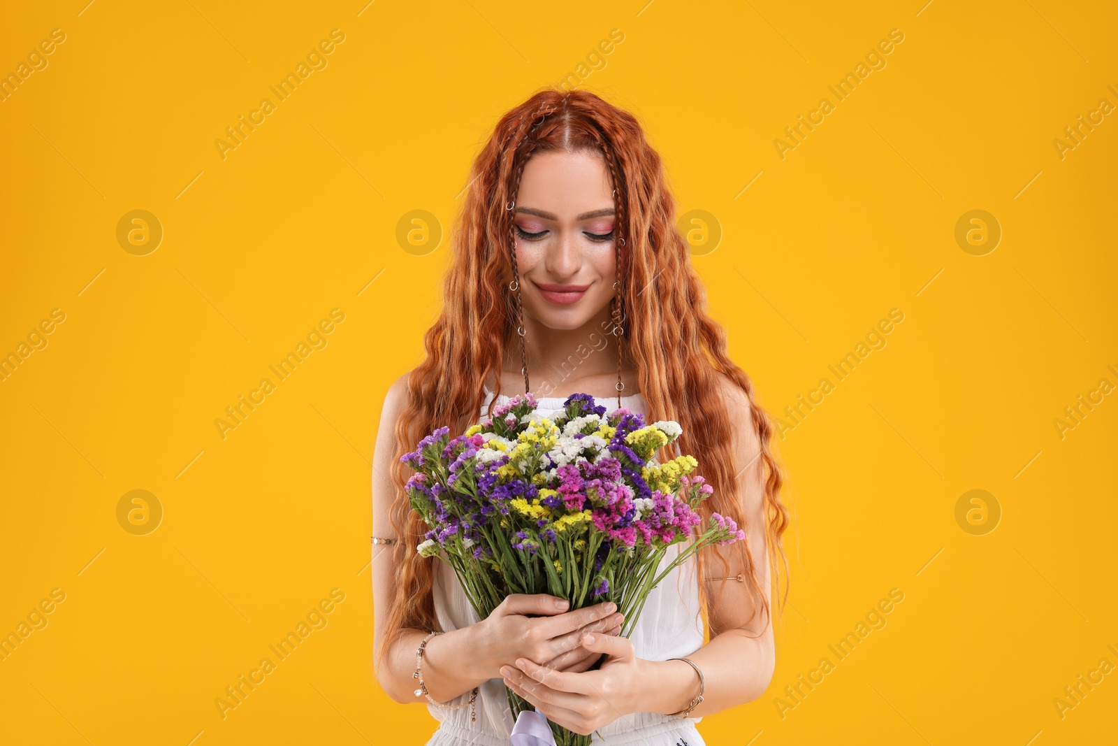Photo of Beautiful young hippie woman with bouquet of colorful flowers on orange background