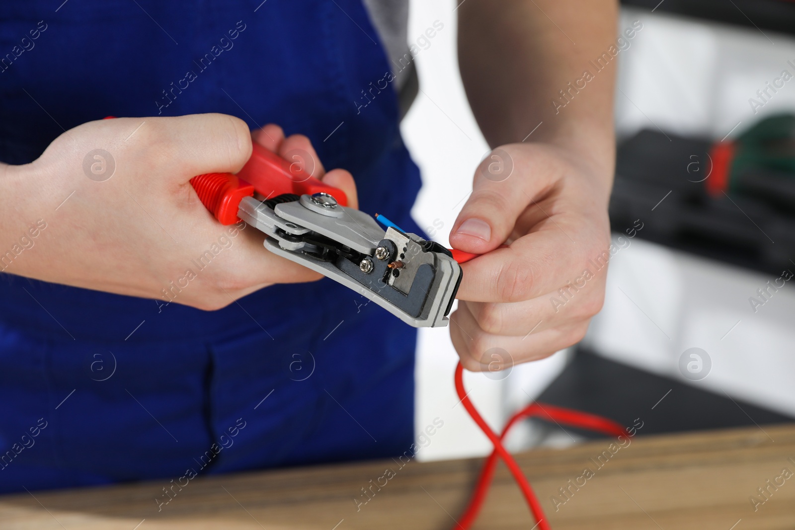 Photo of Professional electrician in uniform stripping wiring indoors, closeup