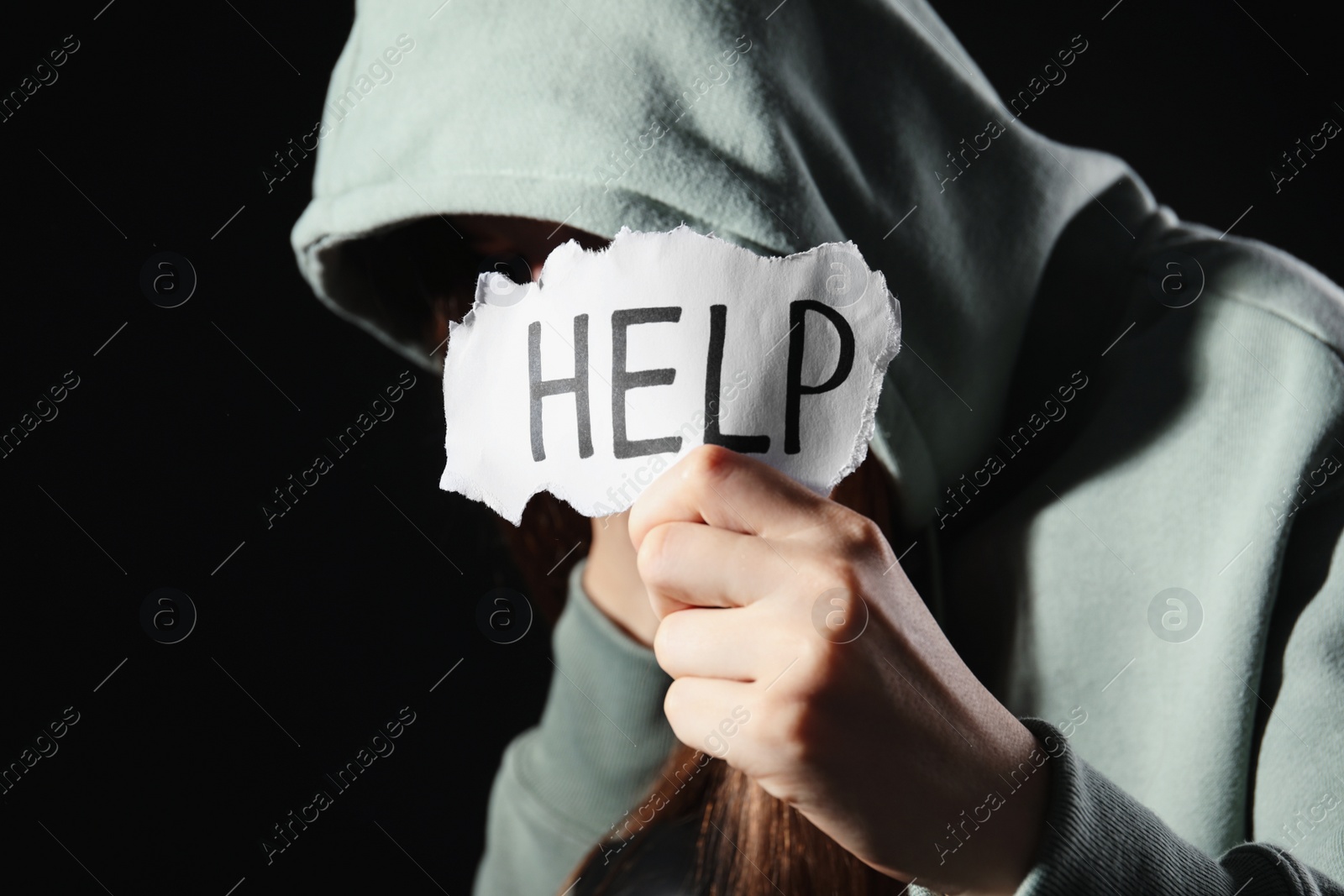 Photo of Woman holding piece of paper with word Help on black background, closeup. Domestic violence concept