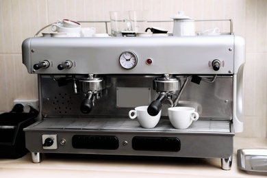 Photo of Modern electric coffee machine with portafilters and cups on table indoors
