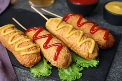 Photo of Delicious deep fried corn dogs with lettuce and sauces on grey table, closeup