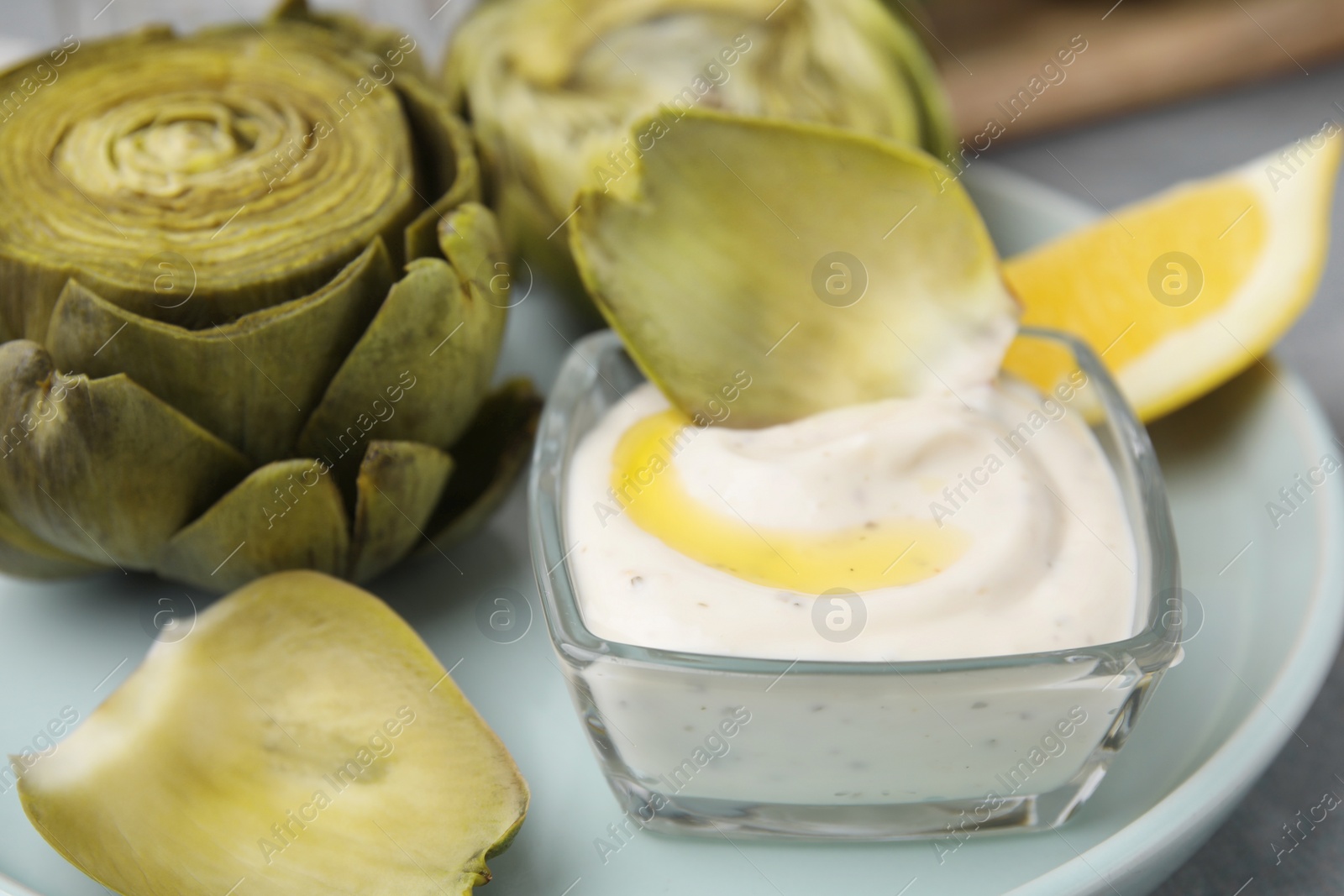 Photo of Delicious cooked artichokes with tasty sauce on plate, closeup
