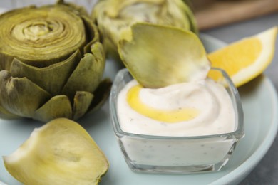 Delicious cooked artichokes with tasty sauce on plate, closeup