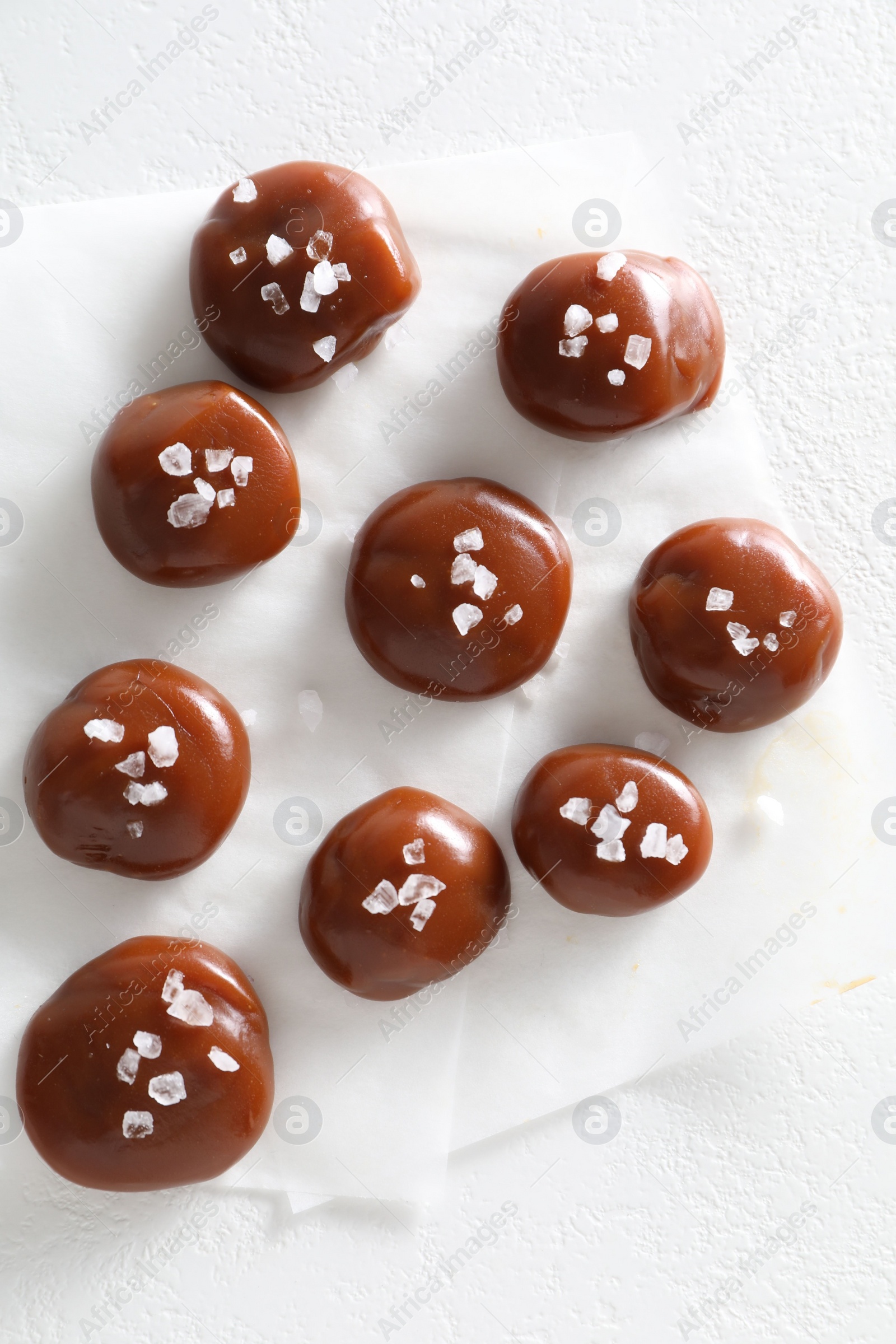 Photo of Tasty caramel candies and salt on white table, top view