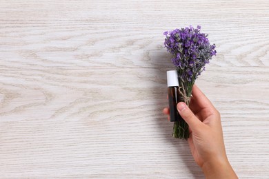 Photo of Woman with bottle of lavender essential oil and flowers on wooden background, closeup. Space for text