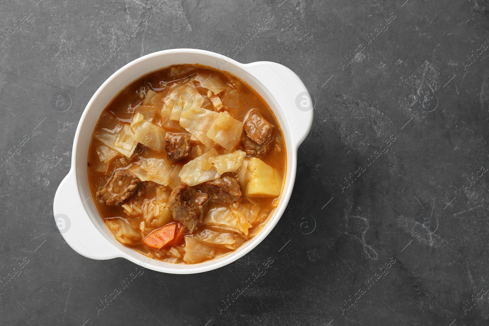 Photo of Tasty cabbage soup with meat and carrot on grey table, top view. Space for text