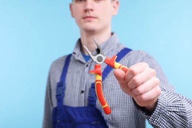 Photo of Young man holding pliers on light blue background, closeup