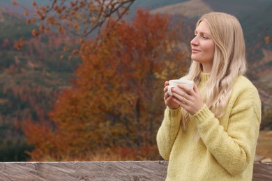 Photo of Young woman with cup of hot drink outdoors in autumn. Space for text