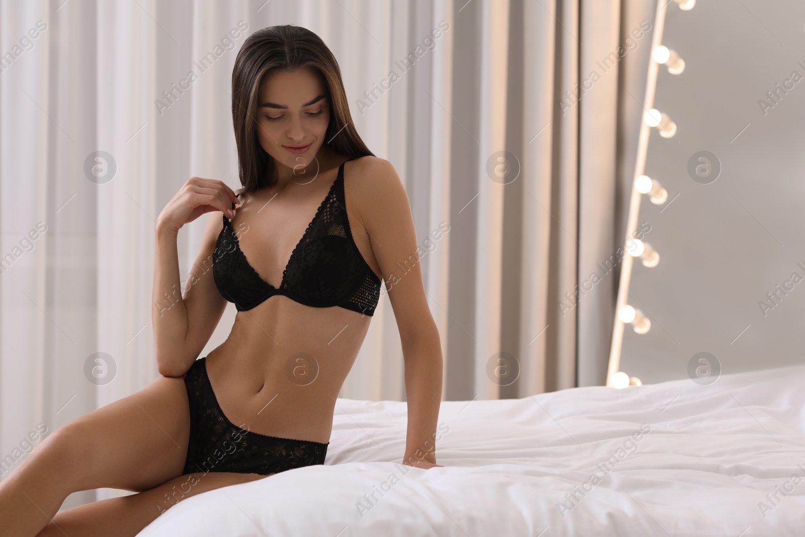 Photo of Young woman in elegant black underwear on bed indoors. Space for text