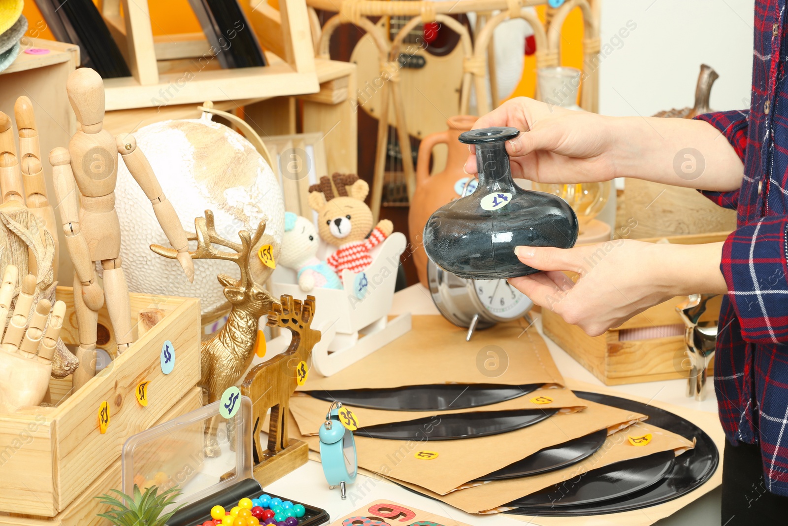 Photo of Woman holding vase near table with different stuff indoors, closeup. Garage sale