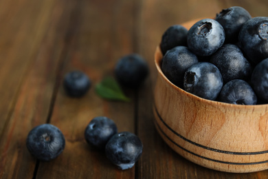 Fresh ripe blueberries in bowl on wooden table, closeup. Space for text