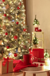 Photo of Red cup on white table in room with Christmas tree. Festive interior design