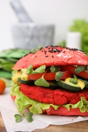 Tasty pink vegan burger with vegetables, patty and microgreens on wooden table, closeup