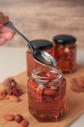 Photo of Woman taking spoon of honey from glass jar with nuts at table, closeup