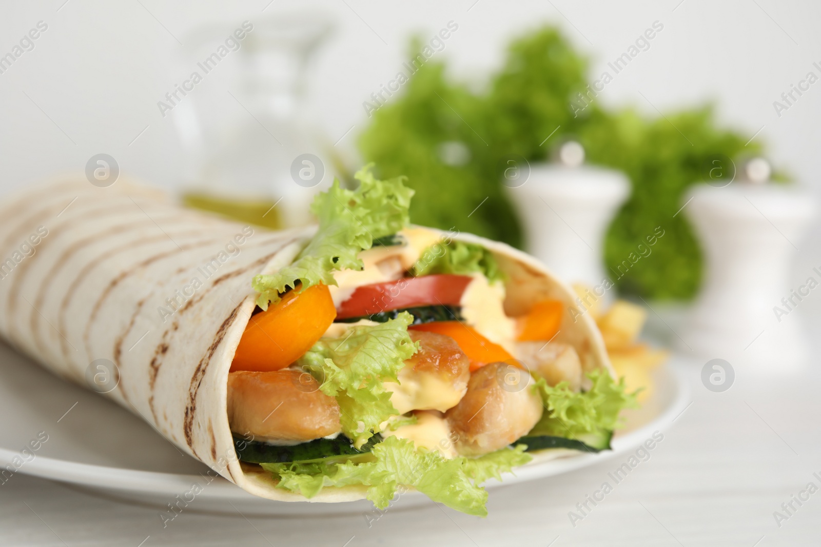 Photo of Delicious shawarma with chicken meat and fresh vegetables served on white wooden table, closeup