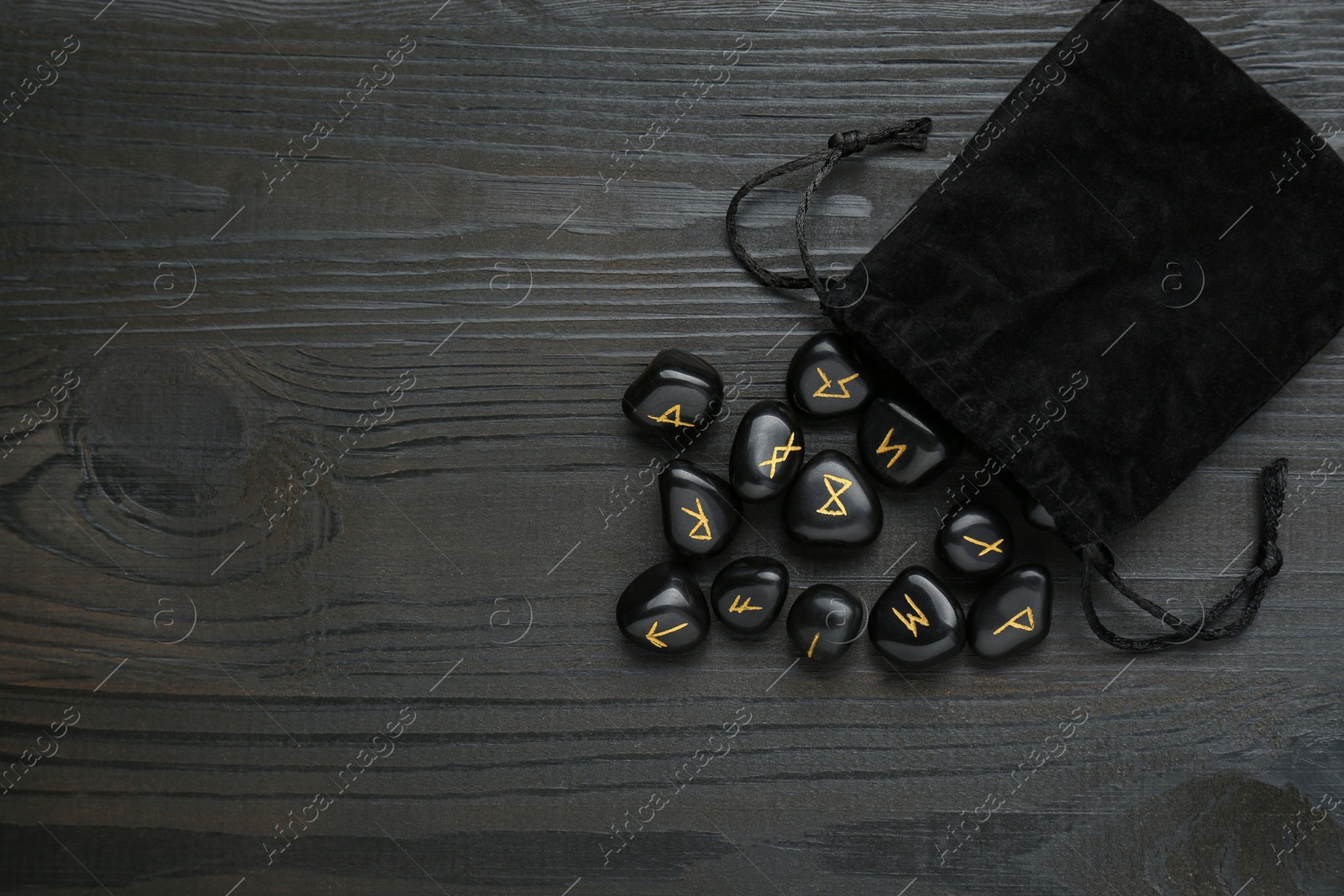 Photo of Bag with rune stones on black wooden table, flat lay. Space for text