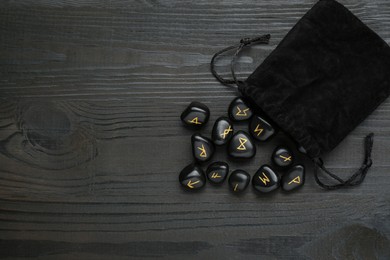 Bag with rune stones on black wooden table, flat lay. Space for text