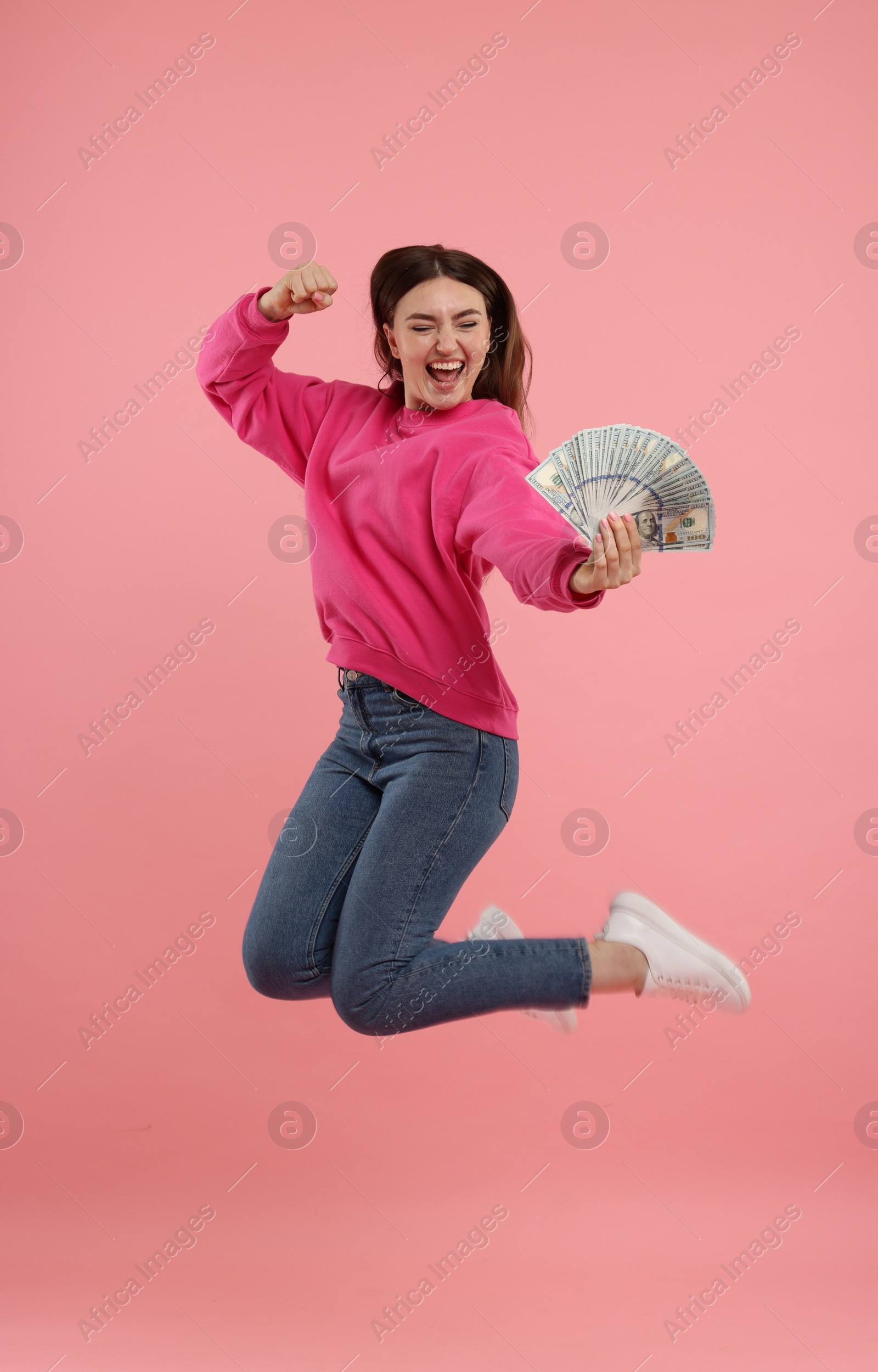 Photo of Happy woman with dollar banknotes jumping on pink background