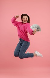 Happy woman with dollar banknotes jumping on pink background