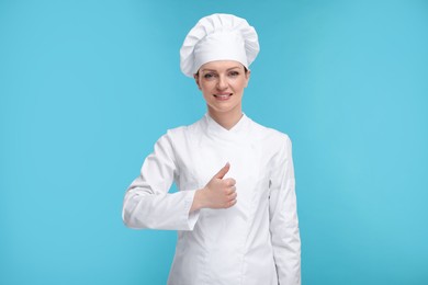 Happy chef in uniform showing thumbs up on light blue background