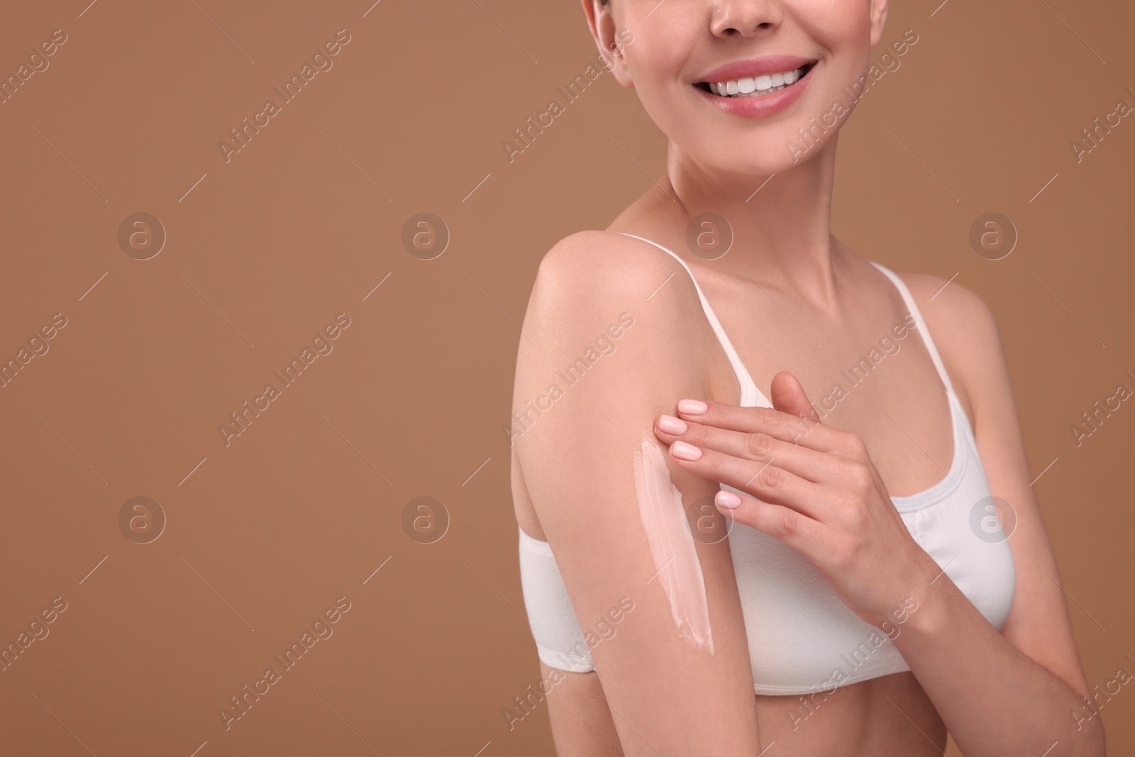 Photo of Woman with smear of body cream on her arm against light brown background, closeup. Space for text