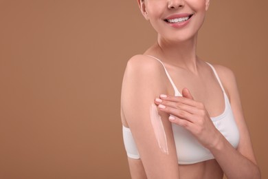Woman with smear of body cream on her arm against light brown background, closeup. Space for text