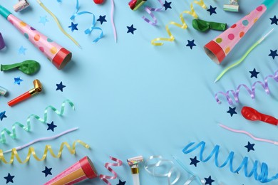 Frame of colorful serpentine streamers and other party accessories on light blue background, flat lay. Space for text