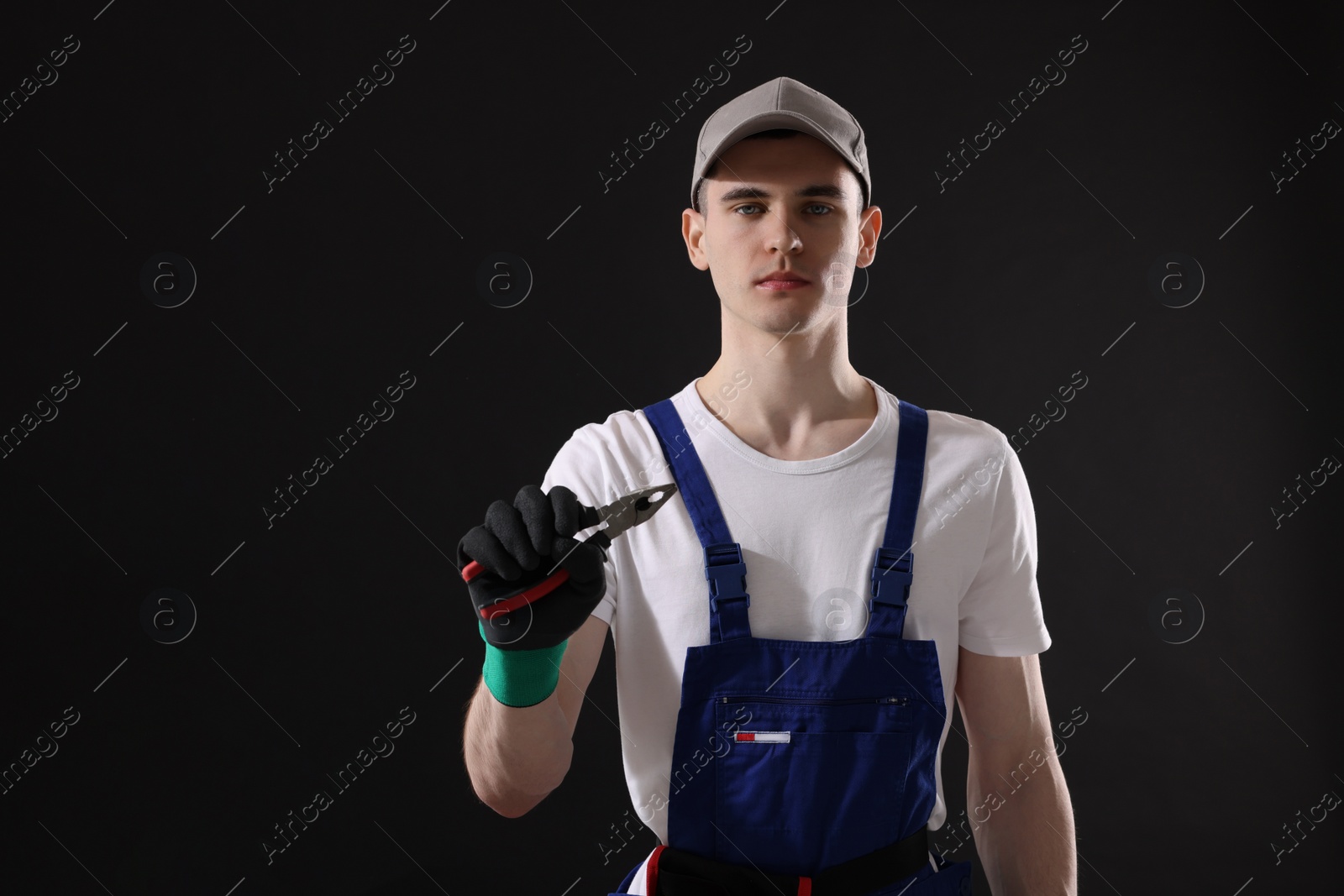 Photo of Young man holding pliers on black background, space for text