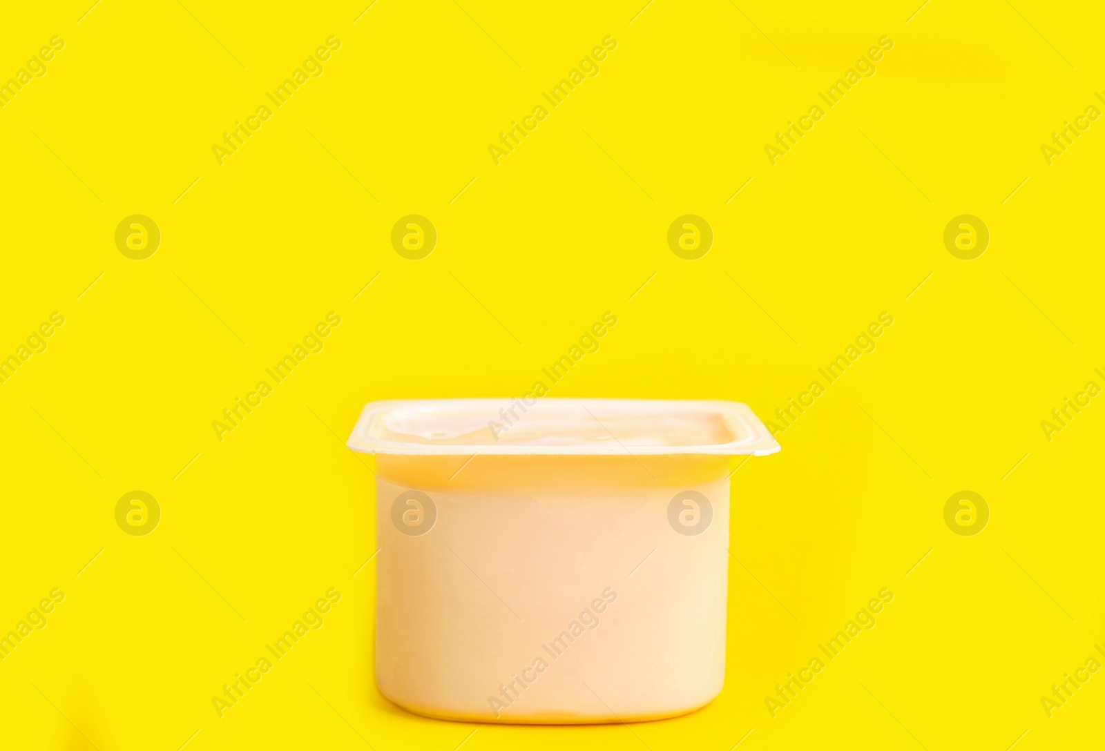 Photo of Tasty organic yogurt in plastic cup on yellow background